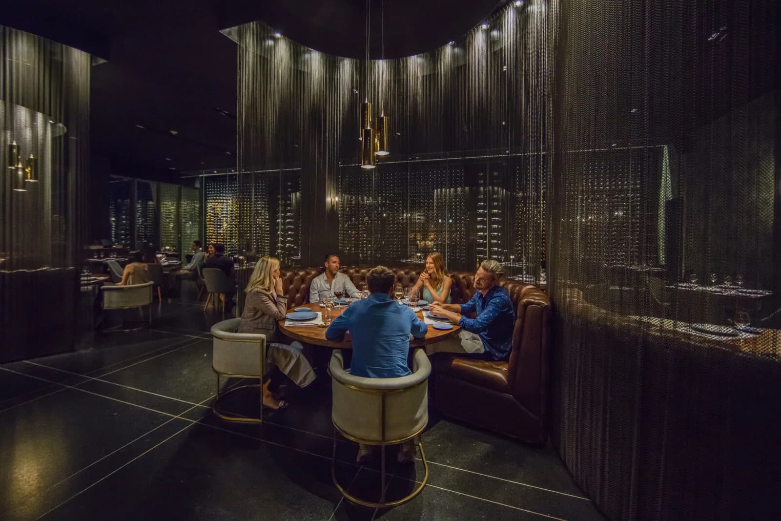 A group of friends gathered around a long dinner table at night, mid-conversation.