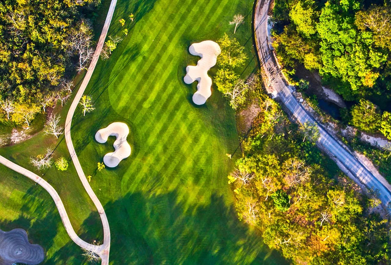 Top-down aerial of a striped Buenaventura fairway with two sculpted bunkers, a winding cart path, and dry tropical forest alongside.