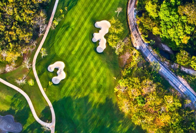 Top-down aerial of a striped Buenaventura fairway with two sculpted bunkers, a winding cart path, and dry tropical forest alongside.
