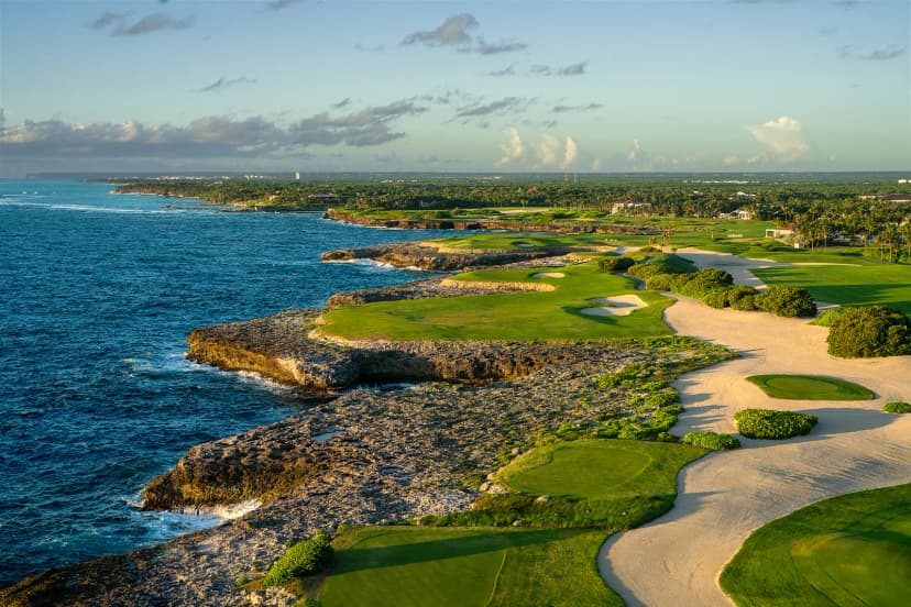 Cliffside holes at Corales Golf Course at sunset, with fairways and bunkers running along a rocky coastline and waves breaking below.