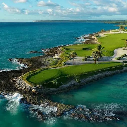 Aerial view of Punta Espada Golf Club, with a green on a rocky peninsula surrounded by turquoise Caribbean water and waves breaking on the coral shore.