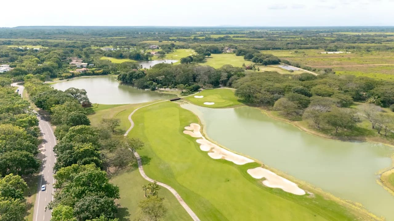 High aerial of Buenaventura Golf Club's fairways curving between lakes, sand bunkers, and trees, with the coastal plain beyond.