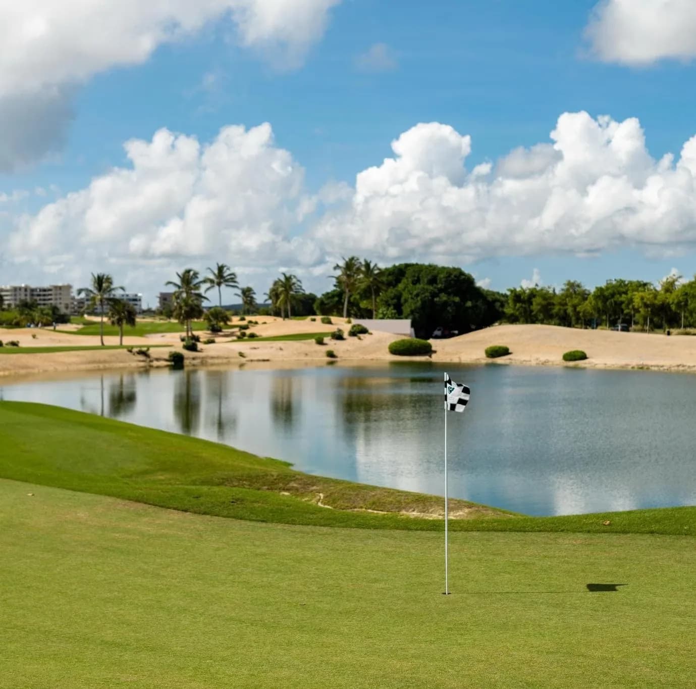 Checkered flag on a lakeside green framed by sand waste areas at Las Iguanas, Cap Cana