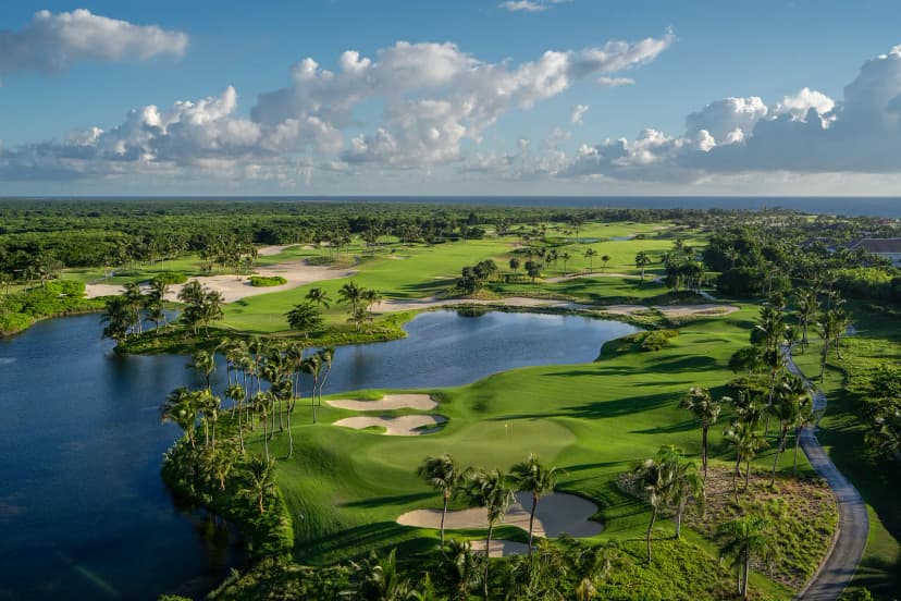Aerial view of Corales Golf Course showing fairways, sand bunkers and lakes lined with palm trees, with the Caribbean Sea on the horizon.