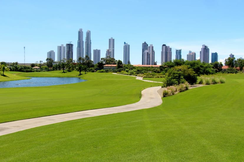 A wide fairway and curving cart path at Santa Maria Golf Club beside a lake, with Panama City skyscrapers in the distance.