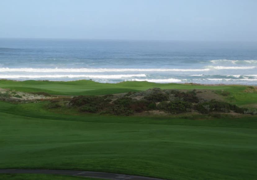 The first-hole fairway at The Links at Spanish Bay with dune scrub and Pacific surf breaking beyond.