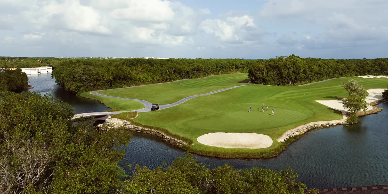 Aerial of an El Camaleón green beside a mangrove canal with a stone cart bridge