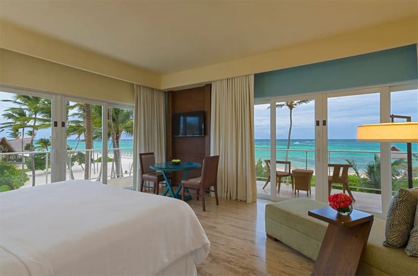 Westin Puntacana corner guest room with wraparound glass doors, a balcony table and the turquoise sea beyond the bed