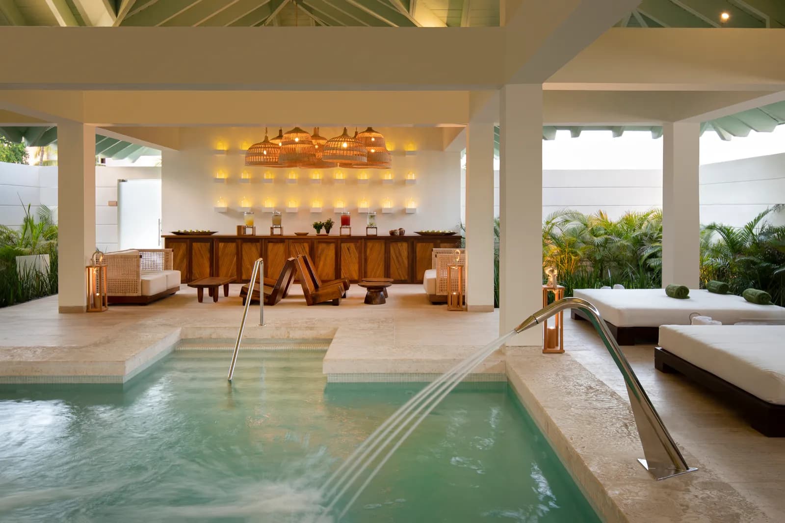 Hydrotherapy pool at Yhi Spa with water jets, daybeds, and a candlelit juice bar under an open-air pavilion.