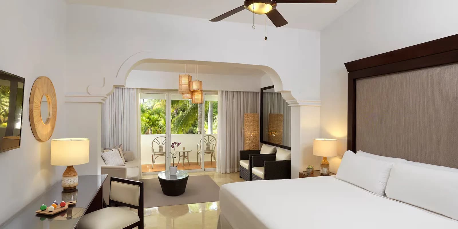 Guest room at Melia Caribe Beach with a king bed, sitting area, and an arched alcove opening to a palm-view balcony.