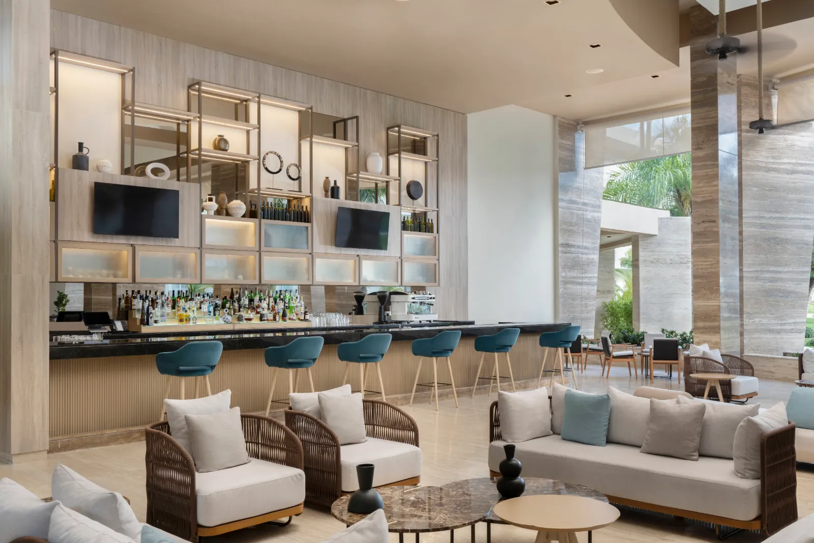 The lobby bar at The Westin Puntacana with teal upholstered barstools, woven armchairs, cream sofas and marble-topped tables.