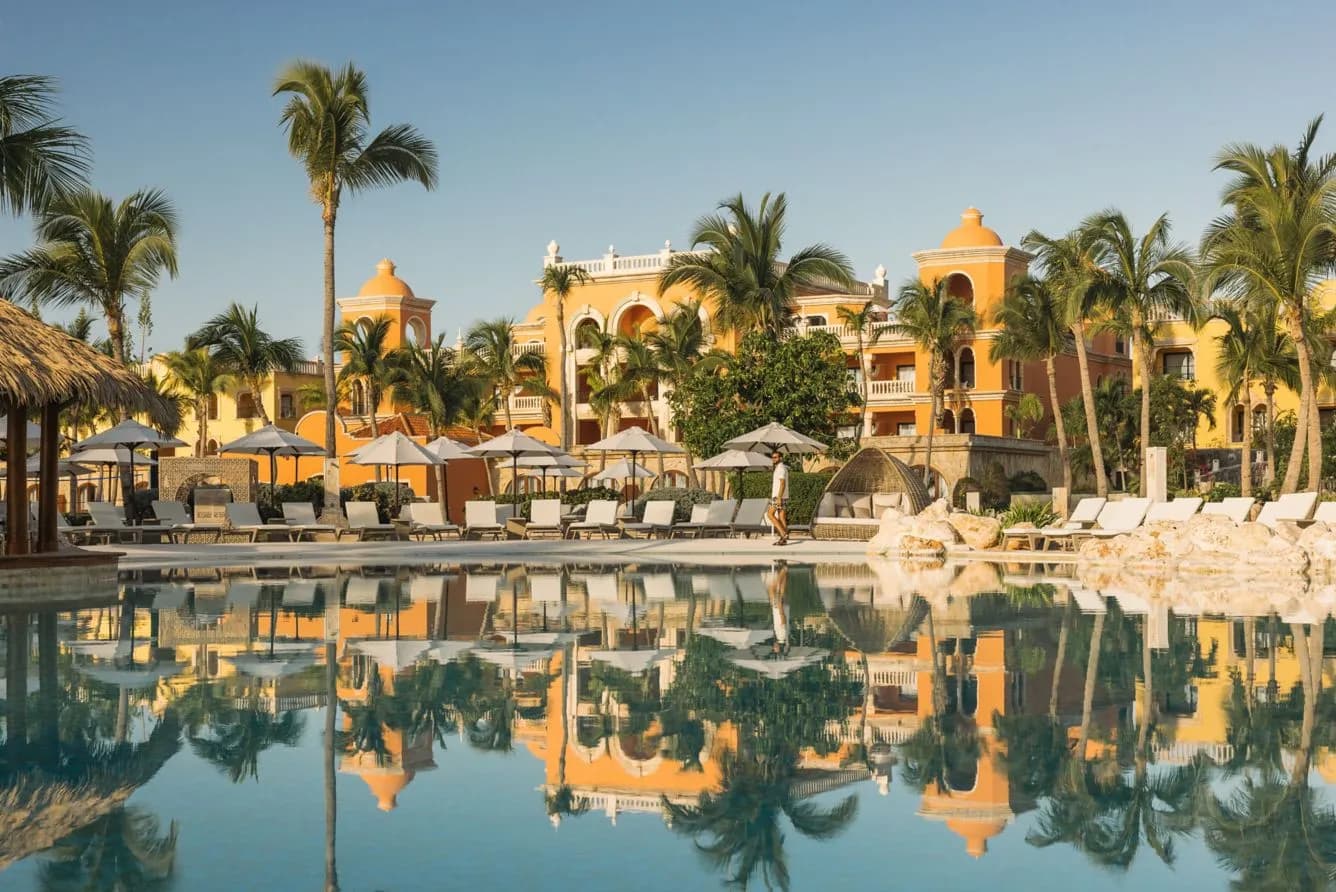 The main pool at Sanctuary Cap Cana at golden hour, reflecting the resort's ochre Spanish colonial towers and palms.