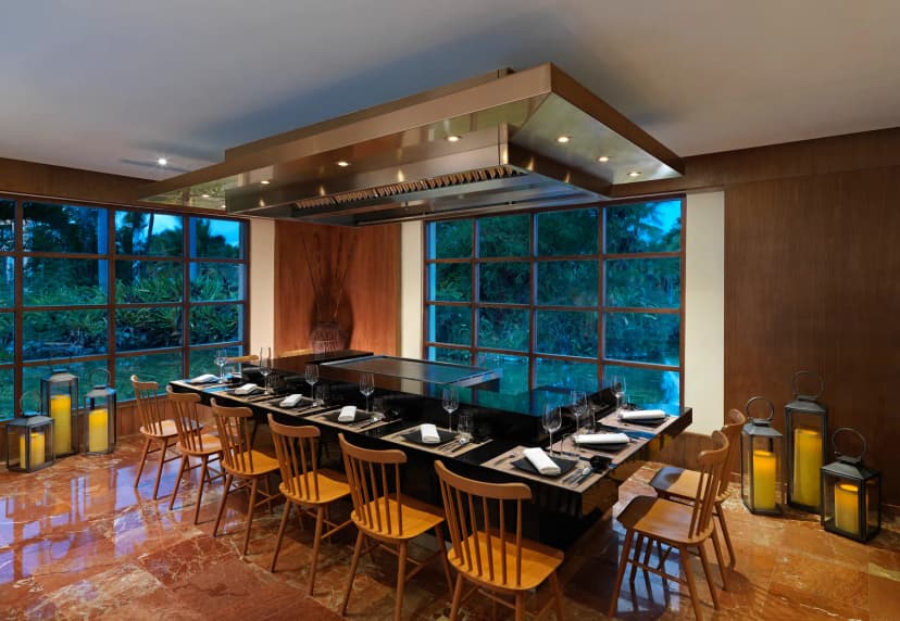 Teppanyaki grill table with twelve wooden chairs at Hokkaido restaurant at Melia Caribe Beach, with lanterns and garden windows