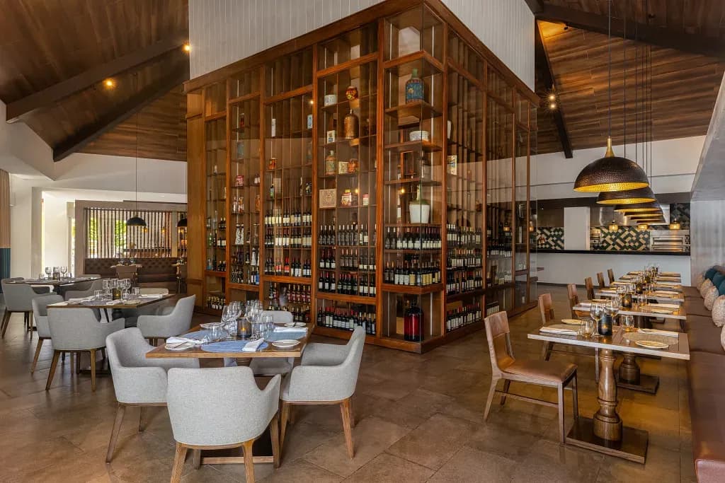 Restaurant interior at Dreams Cap Cana with a two-story glass and wood wine tower, tables set for dinner beneath dark timber ceilings.