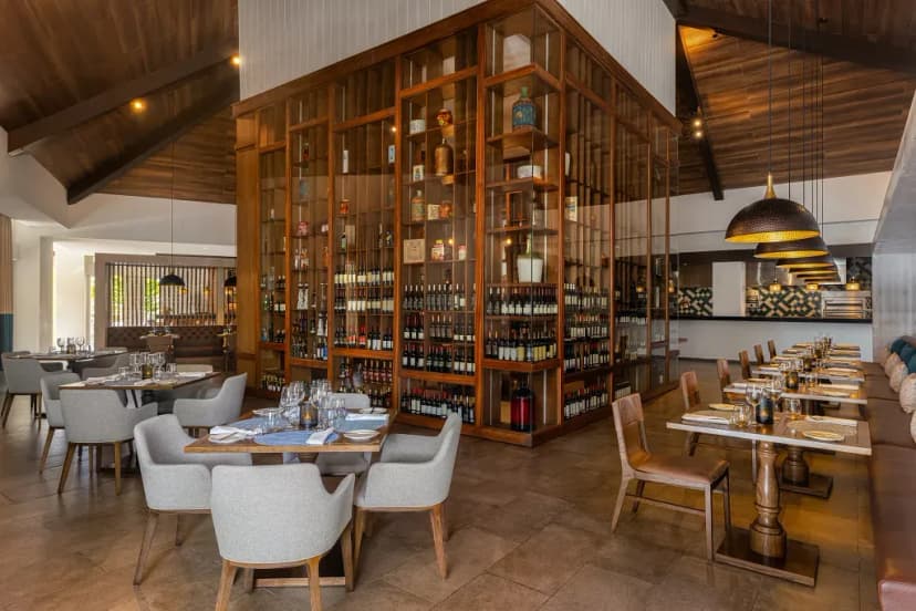 Restaurant interior at Dreams Cap Cana with a two-story glass and wood wine tower, tables set for dinner beneath dark timber ceilings.