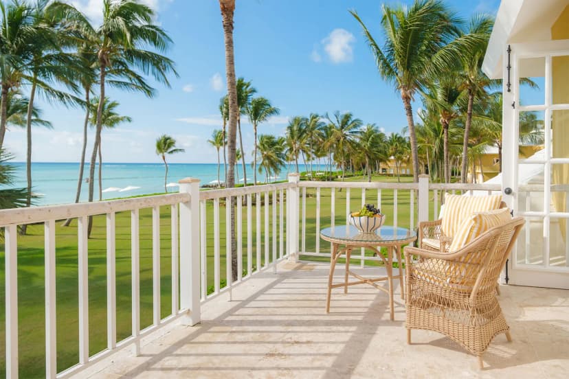 Private balcony of a Junior Suite Ocean View at Tortuga Bay with white railings, wicker furniture, palms, and the turquoise sea beyond.