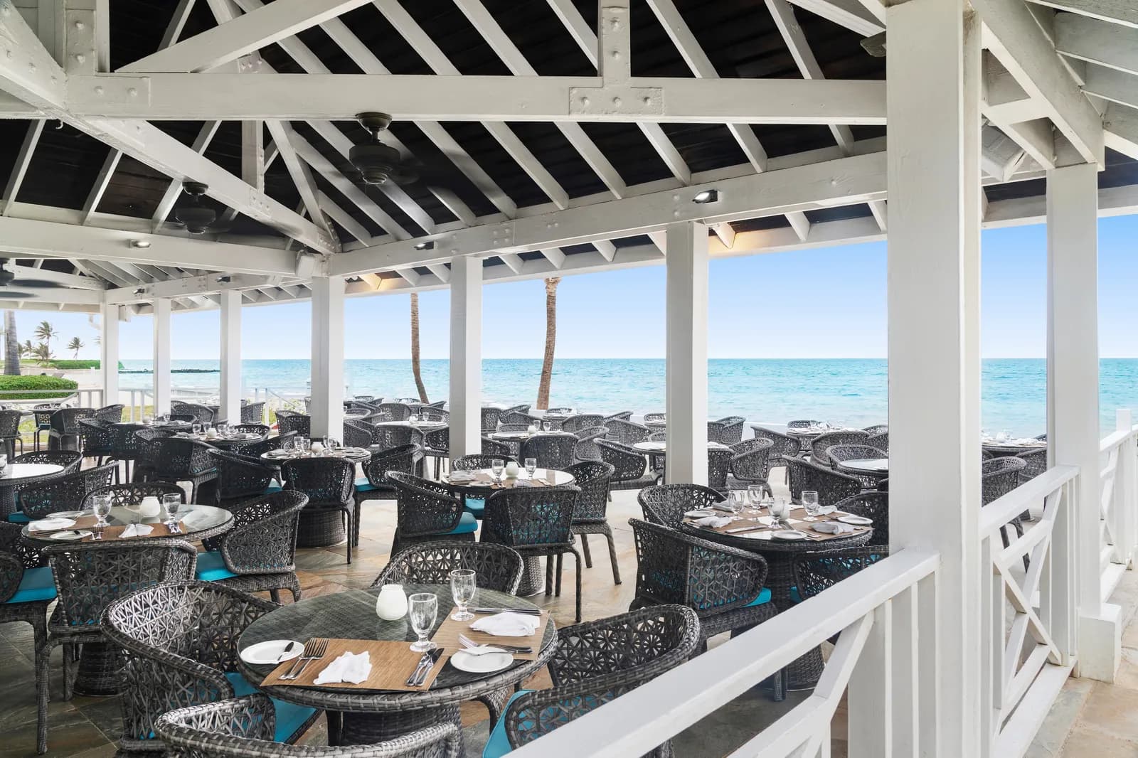 Open-air oceanfront restaurant at Dreams Cap Cana with woven chairs under a white timber pavilion beside the sea.