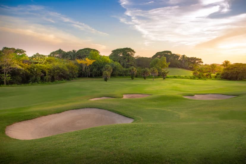 A fairway on the Jack Nicklaus course at Vista Vallarta at sunset, with sand bunkers cut into rolling turf and dense jungle behind.