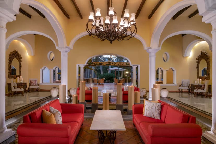 The lobby at Casa Velas, with white archways, a wrought-iron chandelier, red sofas and pillar candles beside shallow reflecting pools.