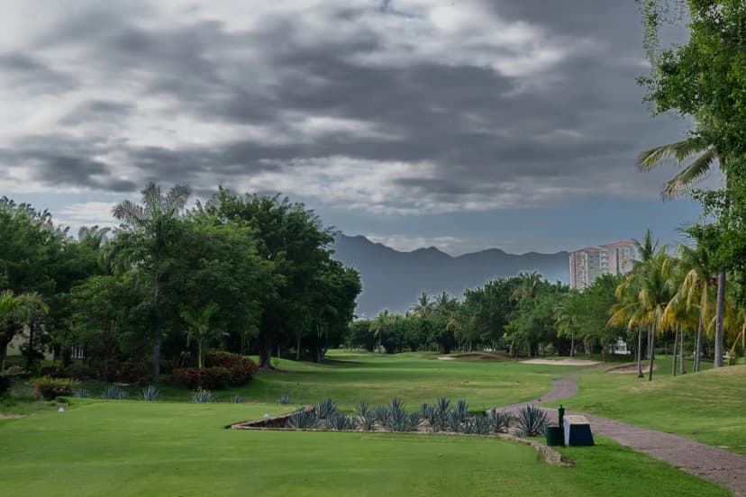 A fairway at Marina Vallarta Golf Club framed by agave plantings and palms, with the Sierra Madre under heavy cloud in the distance.