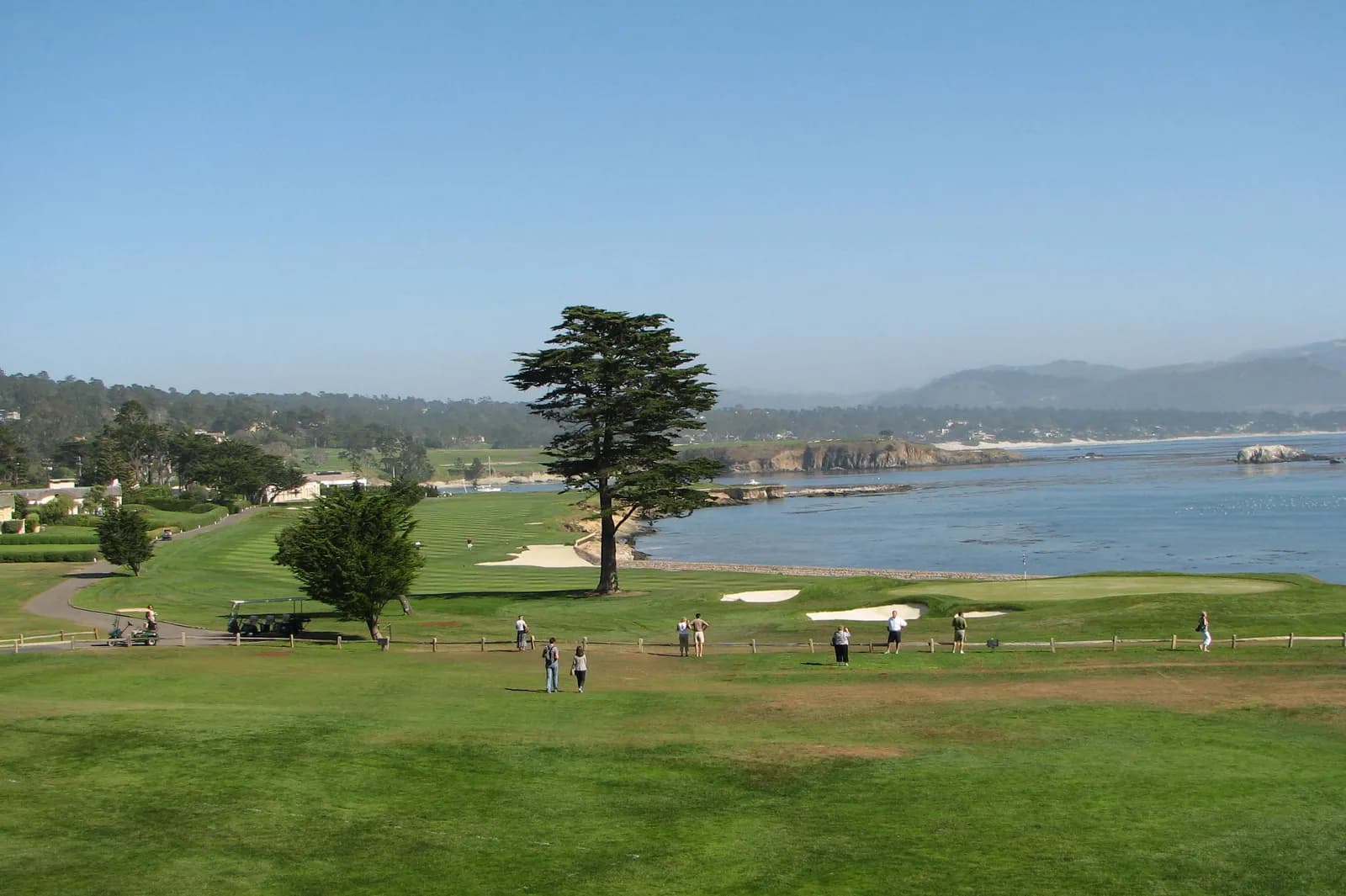 The 18th at Pebble Beach Golf Links curving along the rocky Carmel Bay shoreline, a lone cypress in the fairway and the green beside the sea wall.