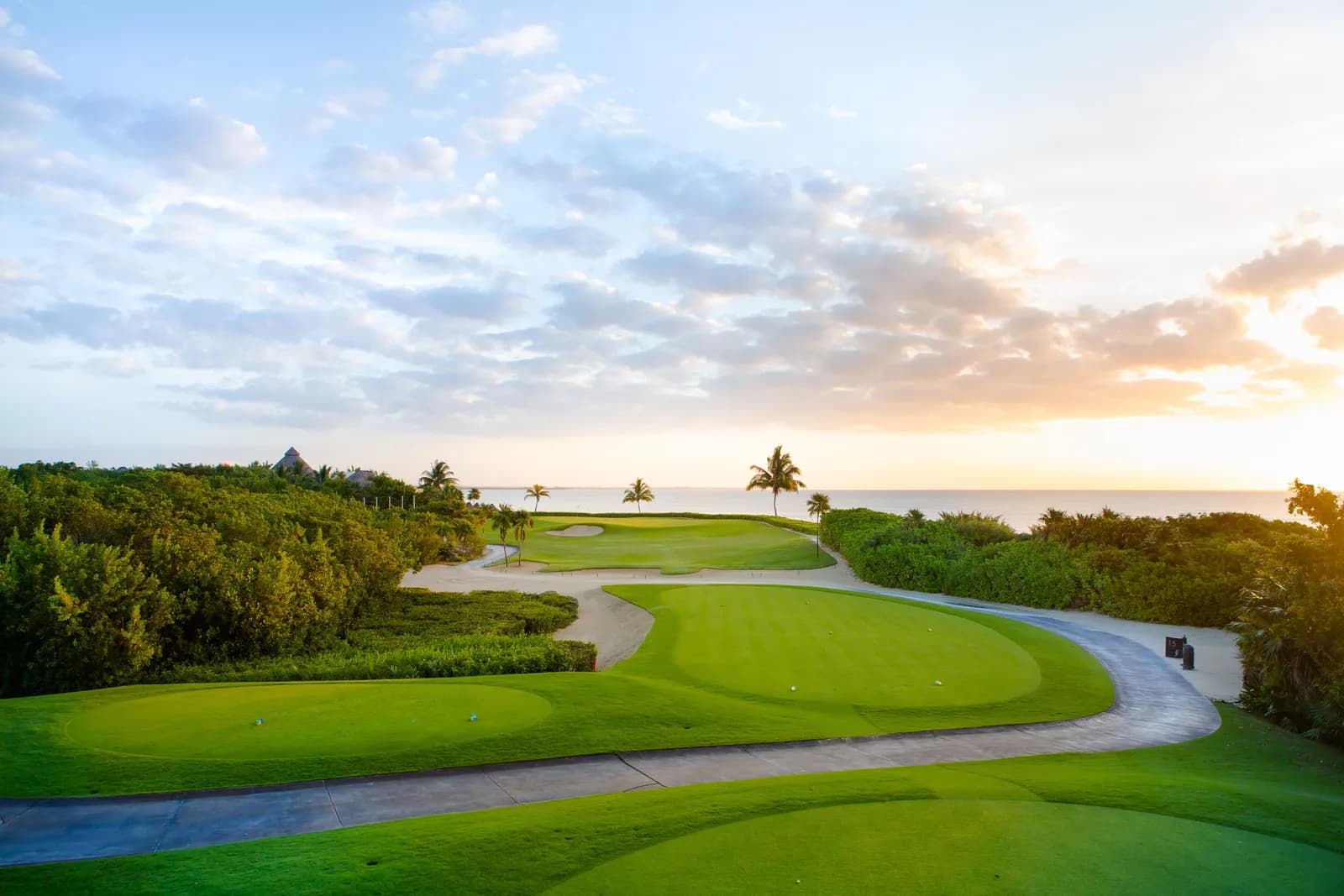 Oceanfront green at El Camaleón at sunrise, bunkers and jungle framing the fairway with the Caribbean on the horizon.