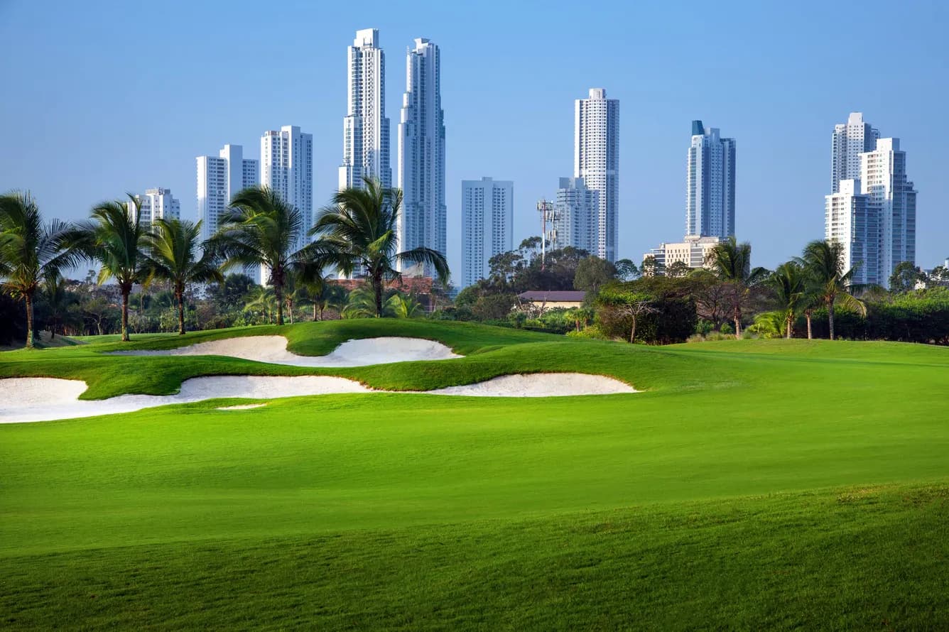 Fairway and sculpted white-sand bunkers at Santa María Golf Club, lined by palms with the Panama City skyline rising behind.